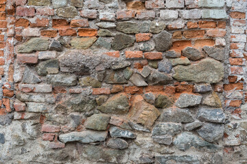 Variety of crumbling red bricks and large, uneven stones on an old, chaotic wall. Rough, uneven, urban, grungy texture with lines of bricks for backgrounds. Graphic design element.
