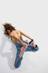 Portrait of young woman lying on floor in weird position, posing in knitted slippers, jeans and top over white background