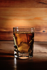A portion of aged alcohol in a glass, close-up against the background of a wooden structure.