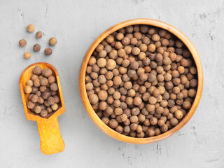 Spice Allspice (Jamaica pepper, Pimento) in wooden bowl and scoop, scattered on gray concrete background. Top view. Healthy eating concept