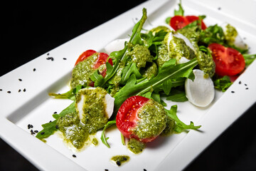 Salad caprese with mozzarella, cherry tomatoes and arugula, seasoned with pesto sauce. Close-up, selective focus