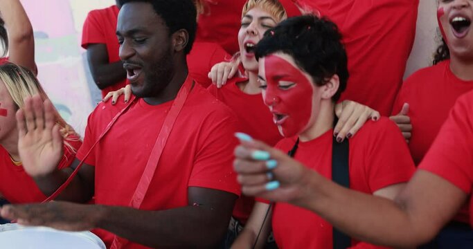Multiracial red sport fans screaming while supporting their team - Football supporters having fun at competion event - World cup conceptconcept