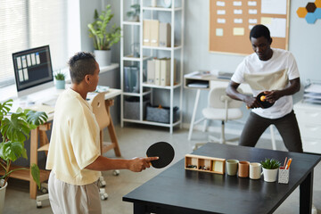 High angle portrait of two African American young people playing table tennis in office, workplace...