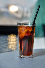 Alcoholic cocktail with cola, ice and lemon on the cafe table