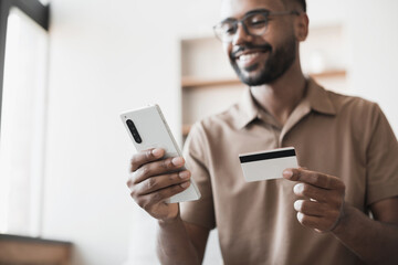Young man holding credit card and using smartphone at home, happy men shopping online, e-commerce, internet banking, spending money, finance concept.