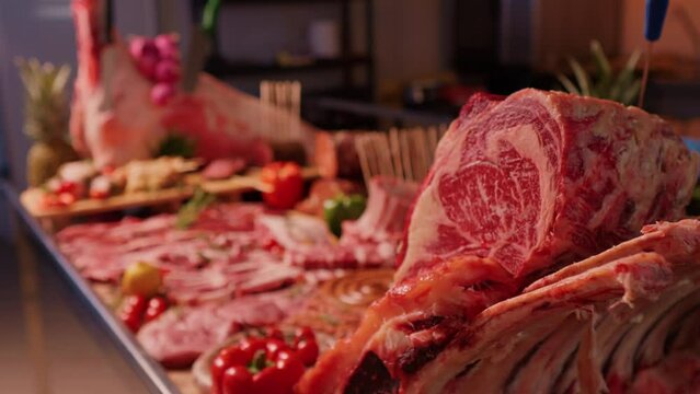 Decorative layout of meat goods on display in a butchers kitchen. Multiple raw and seasoned meat goods set of on a wooden board and metal table.