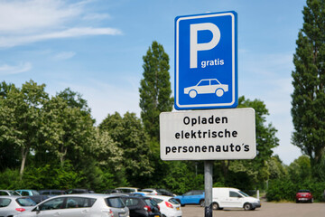 Parking lot in The Netherlands with blue free parking sign and text charging electric passenger cars in the dutch language.