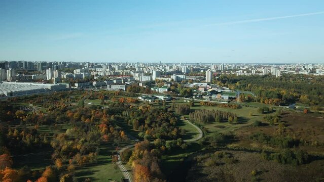 Autumn city park. Trees with colorful leaves. A winding bike path is visible between the trees. City blocks on the horizon. Autumn landscape. Aerial photography.