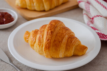 Fresh croissant on white plate and jam on table.