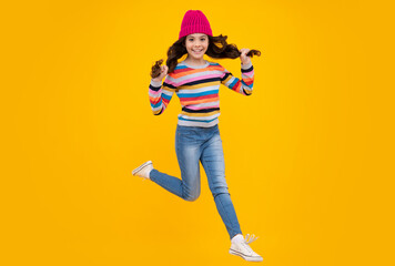 Modern teen girl wearing sweater and knitted hat on isolated yellow background. Jump and run. Happy teenager, positive and smiling emotions of teen girl.