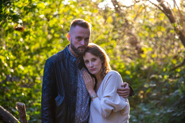 A handsome man tenderly embraces his pregnant wife during an autumn walk in the woods; autumn walk with pregnant woman; pregnant woman's belly; tenderness between partners; love
