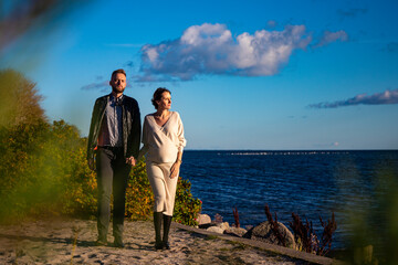 A handsome man tenderly embraces his pregnant wife and shows her love during an autumn coastal walk; autumn walk with pregnant woman; pregnant woman's belly; tenderness between partners; love