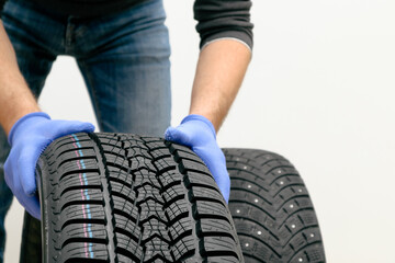 Obraz premium Replacement of winter and summer tires. Mechanic holding a tire at the white background. winter studded tyre, tires replacement