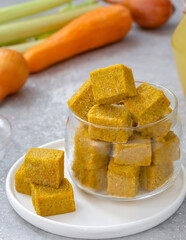 Homemade vegetable bouillon cubes made of braised onion, carrot, celery sticks and salt served in glass jar with ingredients on background. Vertical, selective focus.