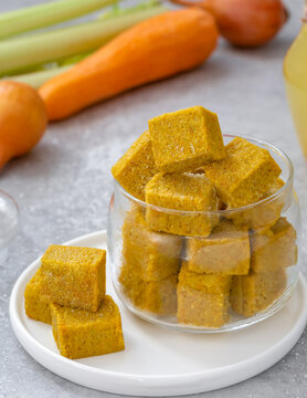 Homemade vegetable bouillon cubes made of braised onion, carrot, celery sticks and salt served in glass jar with ingredients on background. Vertical, selective focus.