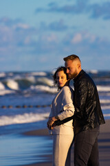 A handsome man tenderly embraces his pregnant wife and shows her love during an autumn coastal walk; autumn walk with pregnant woman; pregnant woman's belly; tenderness between partners; love