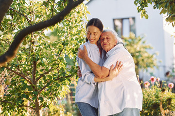 Embracing and posing for a camera. Young woman is with her senior mother is in the garden