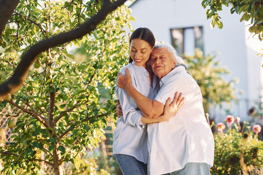 Embracing and posing for a camera. Young woman is with her senior mother is in the garden