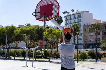 Young muslim man playing street basketball in a city court, throwing ball, training and sport...