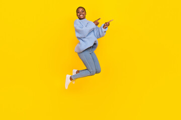 Fototapeta na wymiar Full size photo of young girl jump air directing fingers empty space attention new clothes shop sales isolated on yellow color background