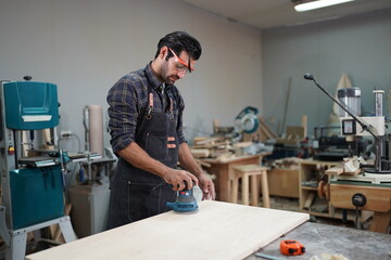 Contemporary Carpenter Working, Portrait of modern carpenter making wood furniture while working in joinery lit by sunlight with factory background on small business concept, copy space