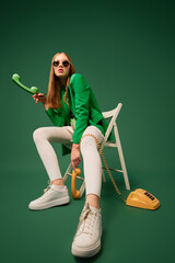 Call your parents. Creative portrait of young without emotions girl in green jacket sitting on...