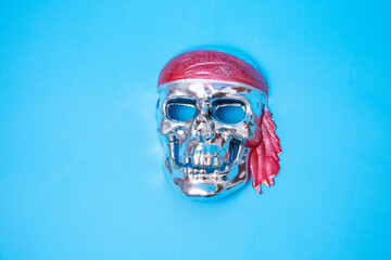 a silver skull with a red headband on a blue background. Halloween, piracy. Jolly Roger. The sign...