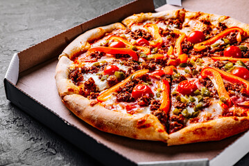 Pizza with Mozzarella cheese, Bolognese sauce, minced meat, pepper, tomato, bacon and vegetables in paper box. Italian pizza on Dark grey black slate background