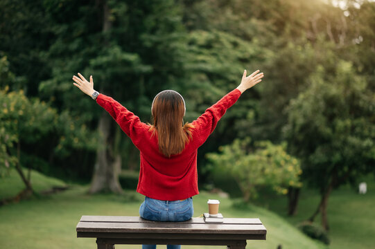 Rear view image of a female traveler sitting and looking at a beautiful park, flowerr field and nature view