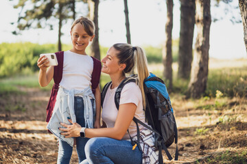 Mother and daughter are taking selfie while enjoy hiking.	