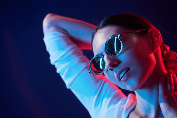Wearing glasses. Portrait of young woman that is indoors in neon lighting