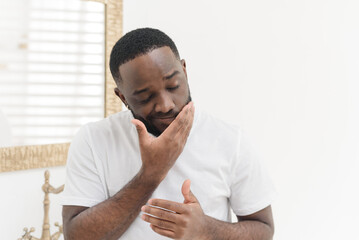 Portrait of young african american man applying nourishing face cream or balm in bathtub, skincare concept