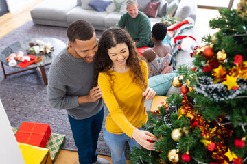 Happy diverse friends decorating christmas tree at home
