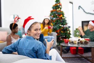 Fototapeta na wymiar Image of happy caucasian woman celebrating christmas at home with friends drinking hot chocolate