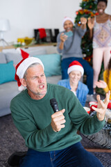 Vertical image of happy caucasian man singing karaoke celebrating christmas with diverse friends