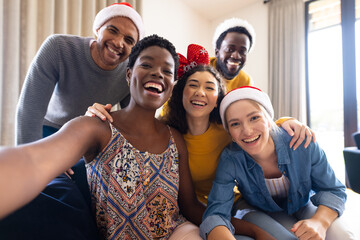Image of happy diverse friends celebrating christmas at home taking selfie
