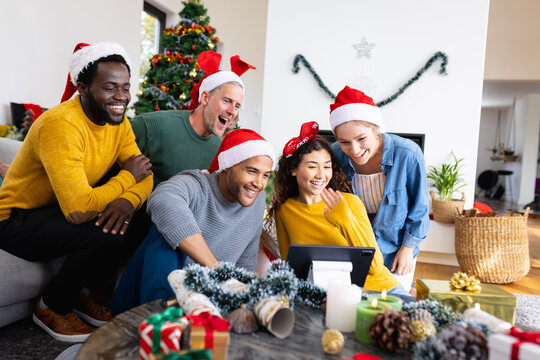 Image of happy diverse friends celebrating christmas at home making tablet video call