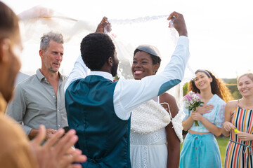 Happy african american couple holding veil and smiling during wedding