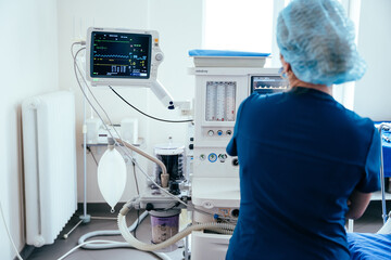 Rear view of female anaesthesiologist with monitor during operating in operation room. Modern equipment in clinic. Emergency room.