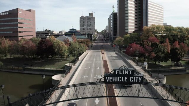 Truck driving on South Saginaw Street in downtown Flint, Michigan showing Vehicle City sign with drone video moving forward.