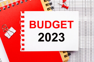 Against the background of the reports, there are red and brown notepads, a white paper clip, red buttons and a white sheet of paper with the text BUDGET 2023. Business concept