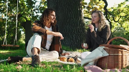 Cheerful young couple drinking hot tea and talking at a picnic in the park outdoors - Powered by Adobe