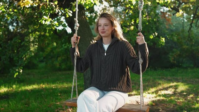 Smiling blonde woman swings on a swing in the sunny park