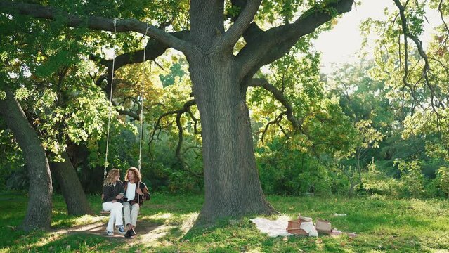 Happy young couple swings on a swing and listening music in headphones in the park