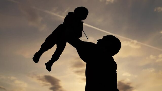 Happy family walks in park outdoors. Father and son silhouette. Parent father throws child into air at sunset. Happy child in hands of his father in park at sunset. Family walking outdoors in the park