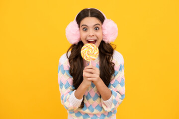 Cool teen child with lollipop over yellow isolated background. Sweet childhood life. Teen girl with yummy lollipop candy. Surprised emotions of young teenager girl.