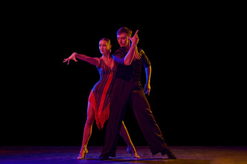 Stylish ballroom dancers couple in gorgeous outfits dancing in sensual pose on dark background in...