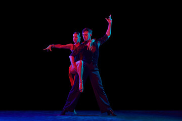 Two dancing people, ballroom dancers in elegance outfits in motion, action over dark background in neon light. Concept of art, music, dance, emotions.