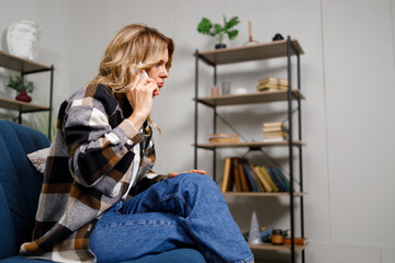 Mature pensive woman talking on phone while sitting on couch indoor