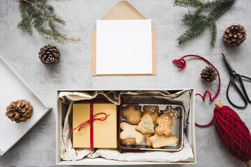 Ein Pakte mit Lebkuchenkeksen und ein Geschenk, ein leerer Brief und Weihnachtsdekoration auf einem grauen Tisch.  - obrazy, fototapety, plakaty